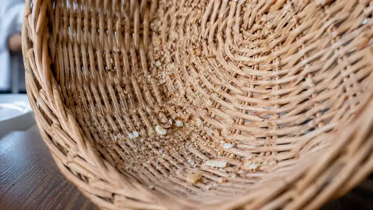 Close-up of a wicker basket tipped sideways with crumbs and a broken cracker spilling out from the weave