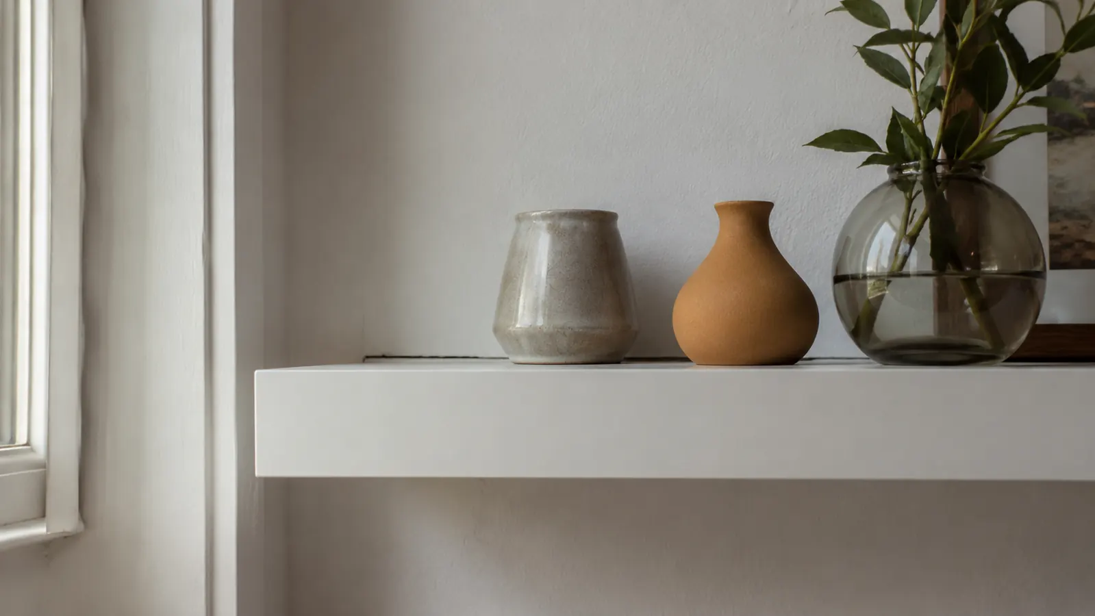 Wall-mounted floating shelf in a hallway with a few decorative objects and books, small drill holes visible in drywall beside it