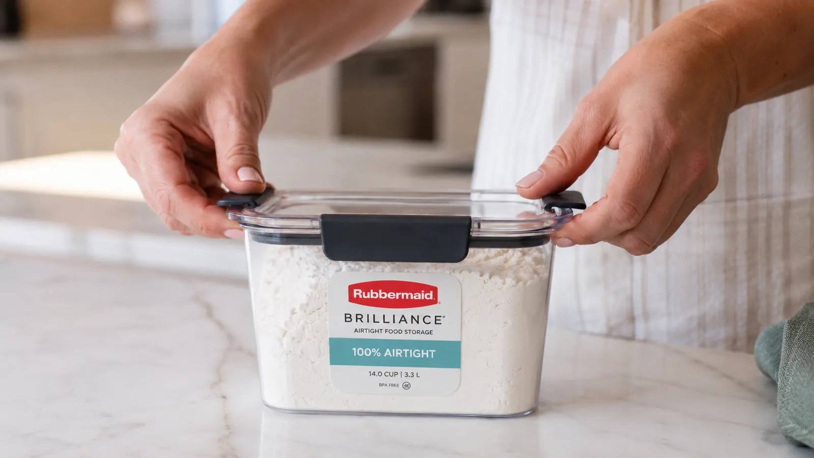 Hands pressing down the four-latch lid on a Rubbermaid Brilliance container filled with flour